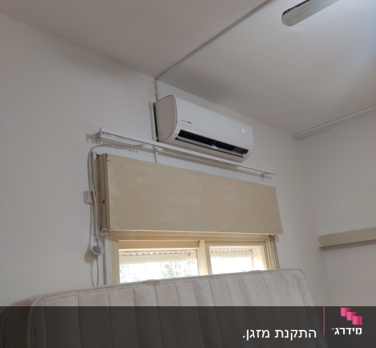 מזגן מותקן על קיר מעל חלון בחדר